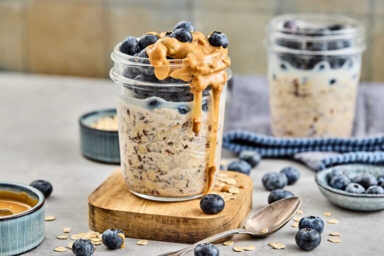 Blueberry almond overnight oats topped with blueberries and dripping almond butter in a mason jar.
