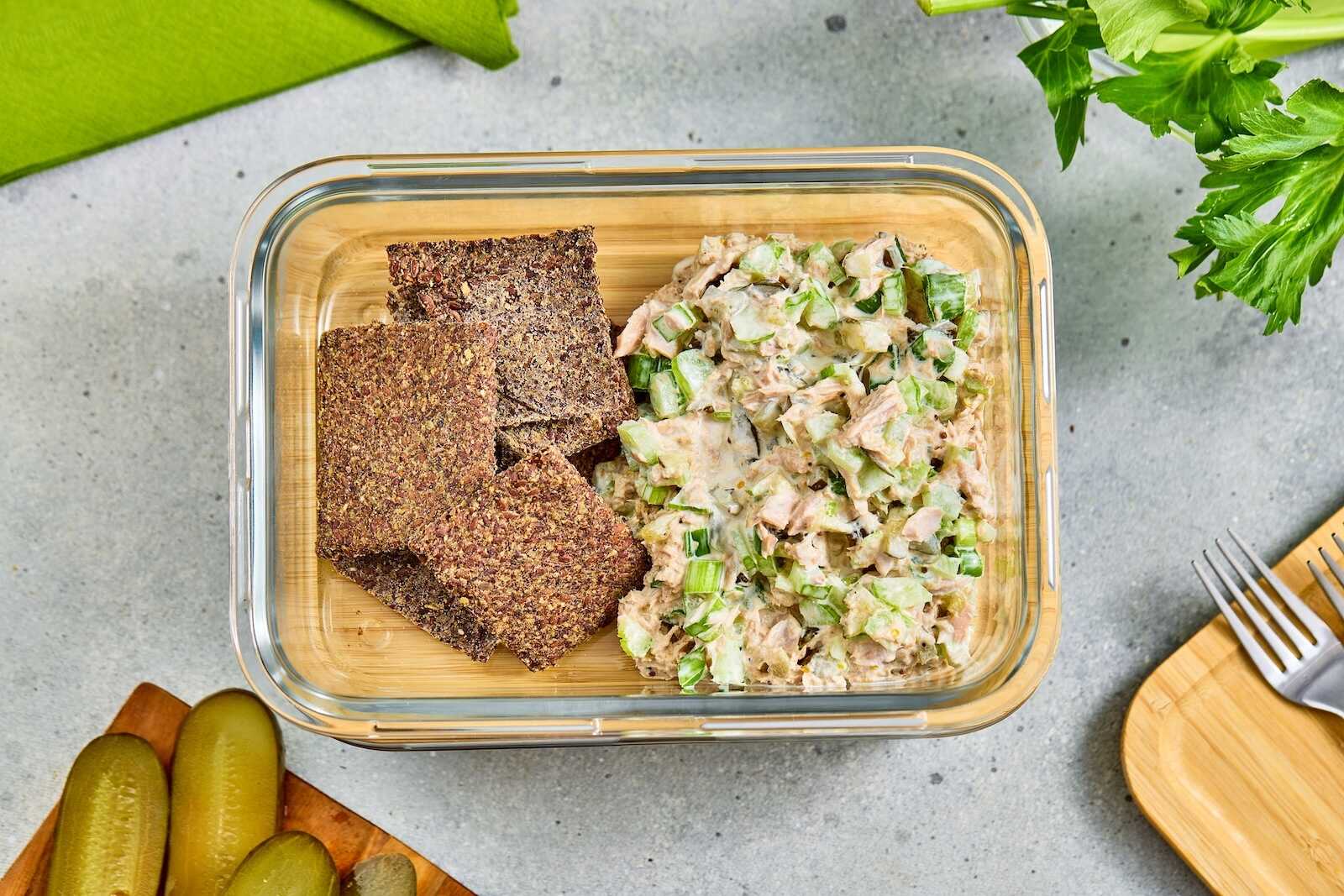 Tuna salad with celery and flaxseed crackers in a glass meal prep container.